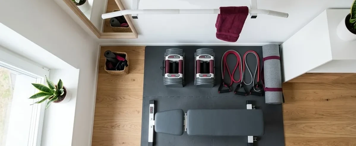 Équipement minimum pour home gym : haltères réglables, bandes de résistance, barre de traction, tapis de sol et banc de musculation